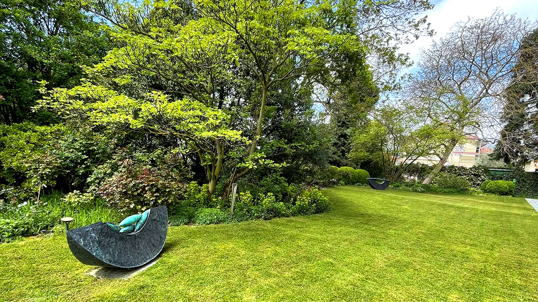Gepflegter Garten mit gemähter Rasenfläche, großen Bäumen und moderner Steinliege in harmonischer Grünanlage