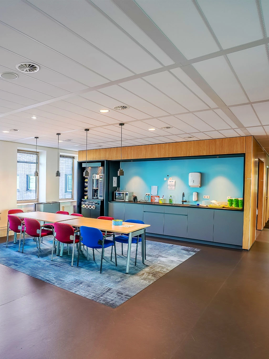 Modernisierter Pausenraum mit Einbauküche, bunten Stühlen und freundlicher Farbgestaltung in einem Bürogebäude.