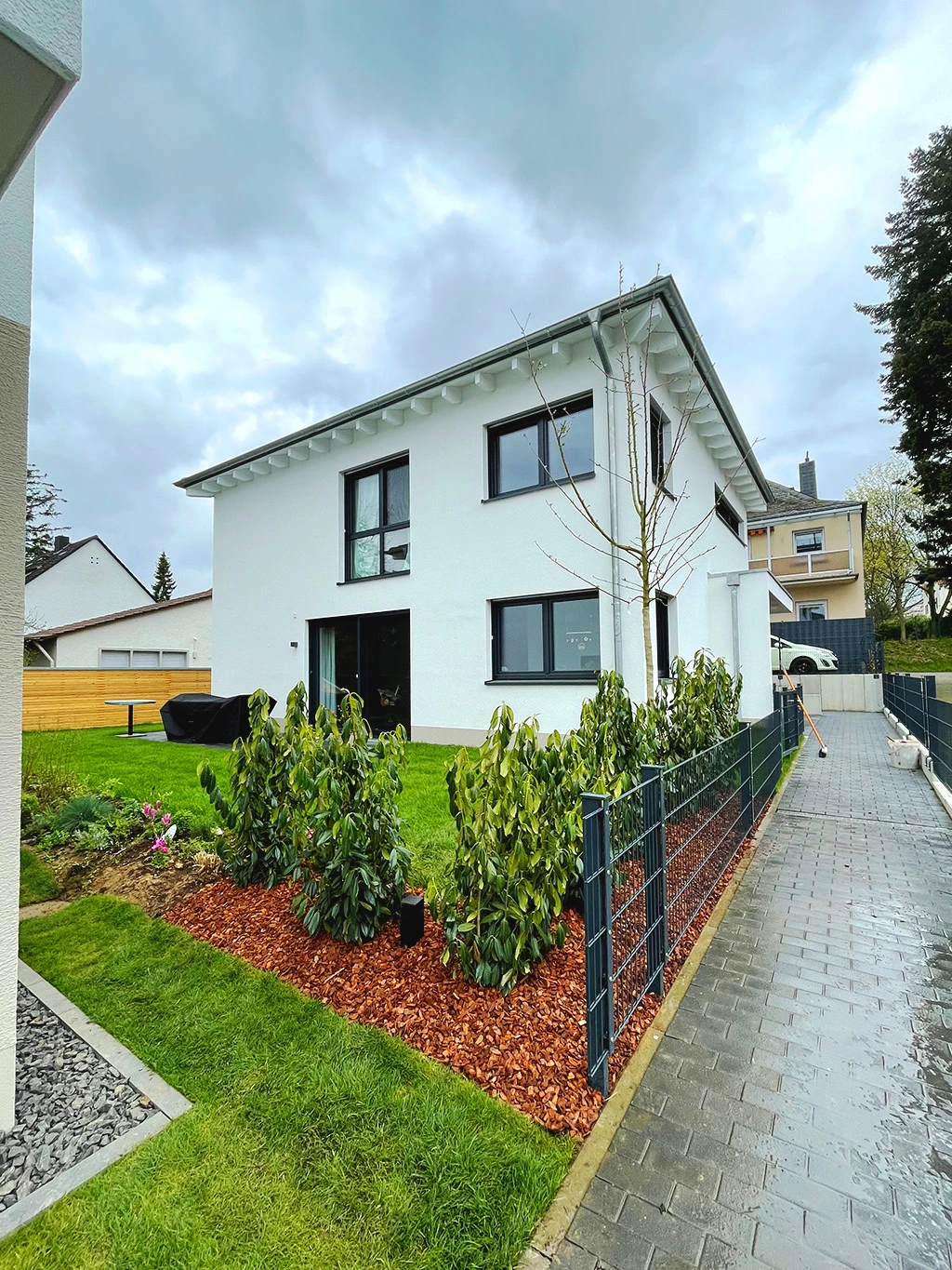 Modernisiertes Einfamilienhaus mit weißer Fassade, sauberer Außenanlage, Zierbeeten und frisch verlegtem Pflasterweg