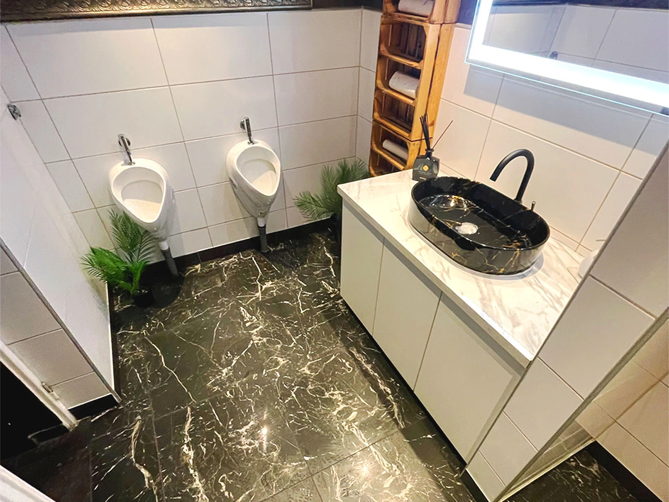 Modernisiertes Herren-WC mit stilvollen Wandfliesen, schwarzem Marmorboden, Designerwaschbecken und beleuchtetem Spiegel