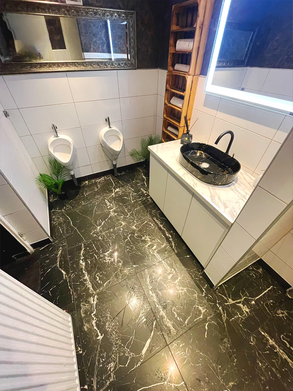 Modernisiertes Herren-WC mit stilvollen Wandfliesen, schwarzem Marmorboden, Designerwaschbecken und beleuchtetem Spiegel
